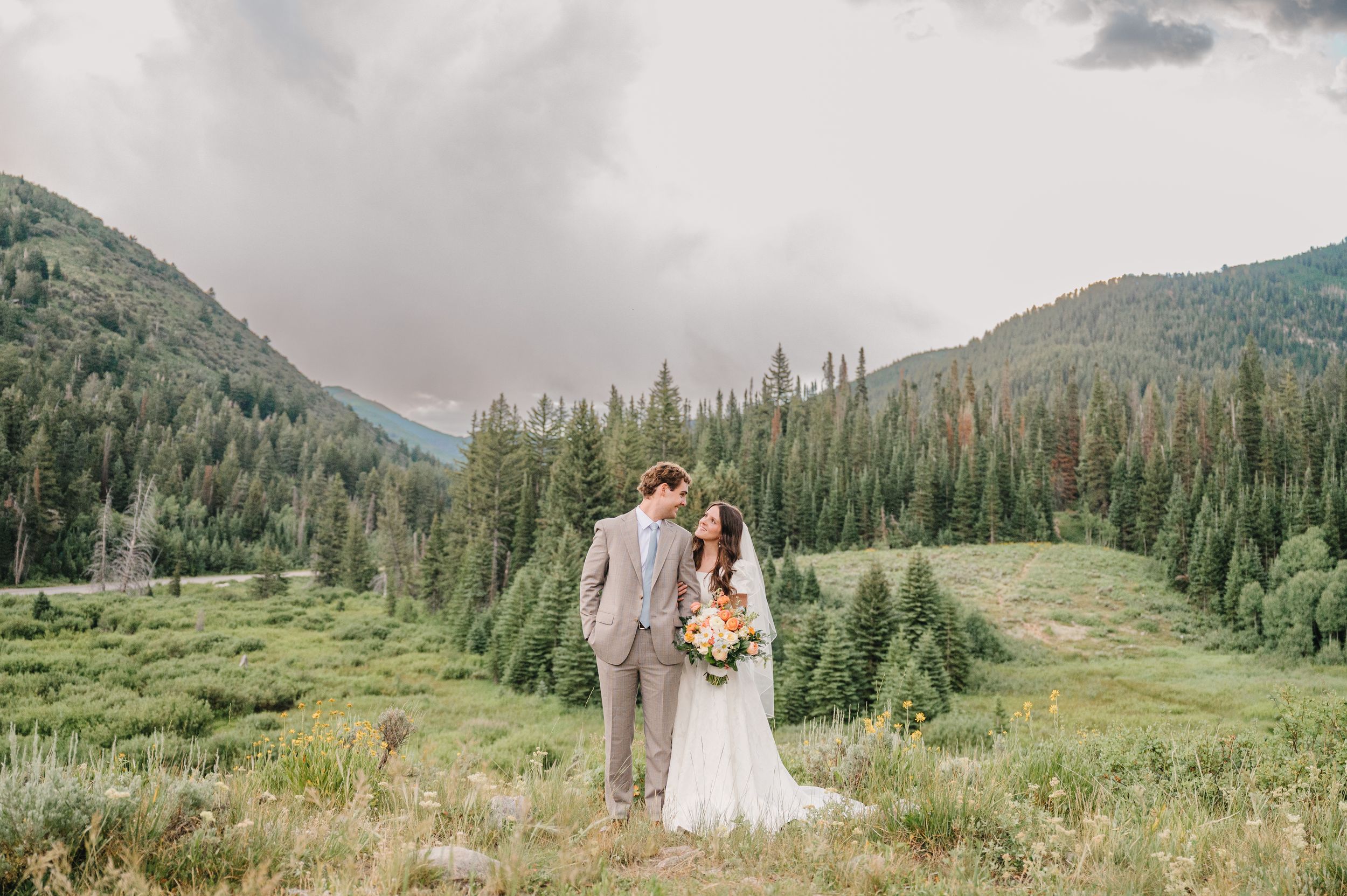A romantic winter scene with two people embracing on tree stumps surrounded by snow-covered evergreen trees.