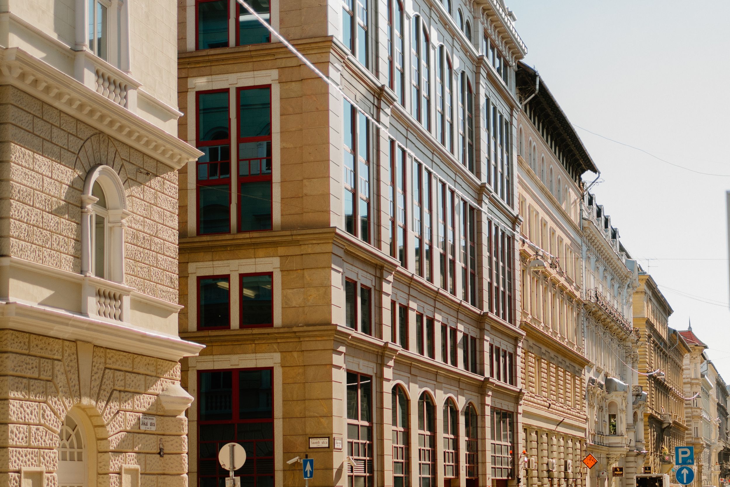 Classic ornate apartment buildings with tall windows line a historic European city street corner on a sunny day.