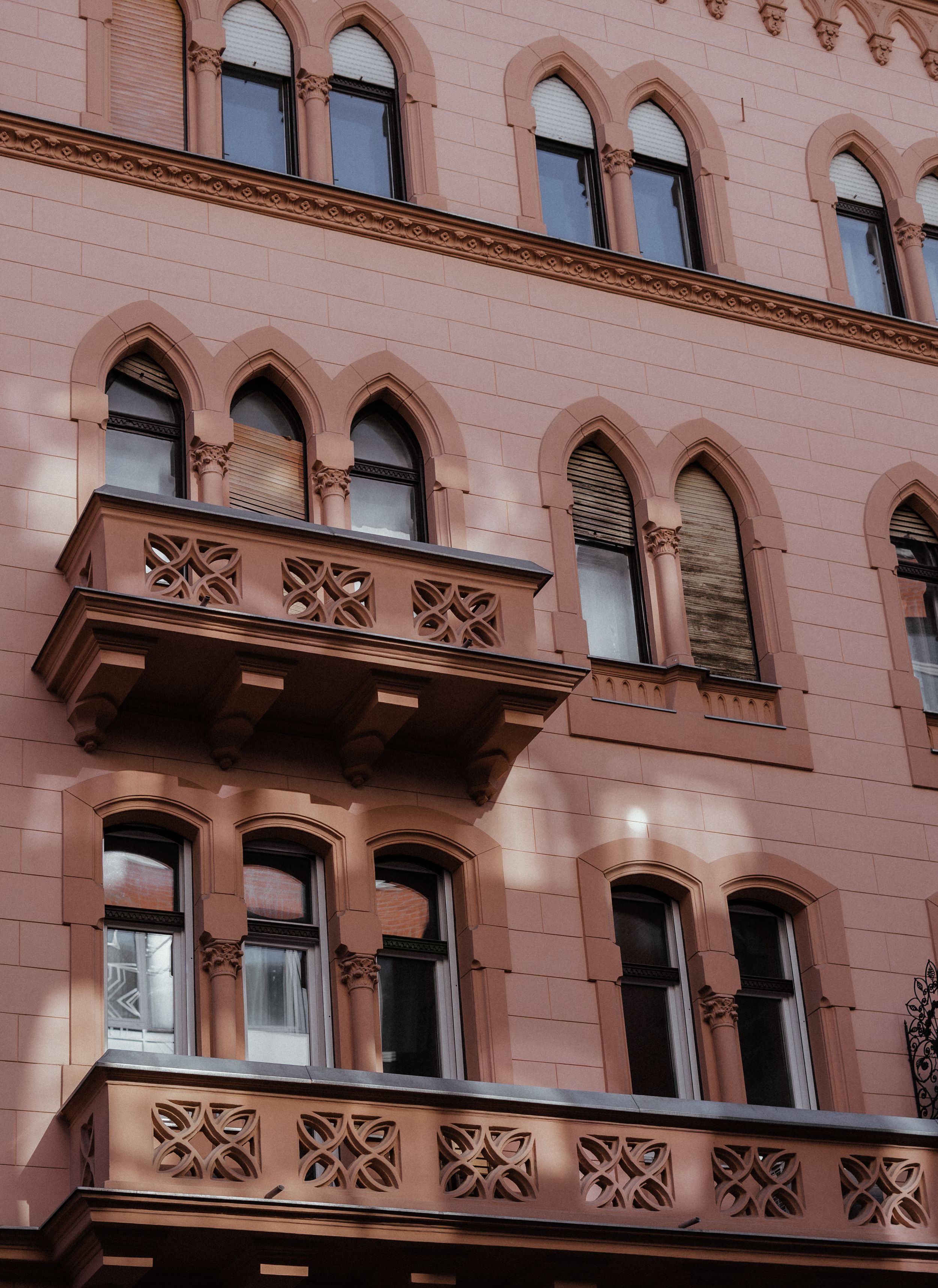 Gothic architectural facade with arched windows and ornate balconies on a pink-colored building exterior.