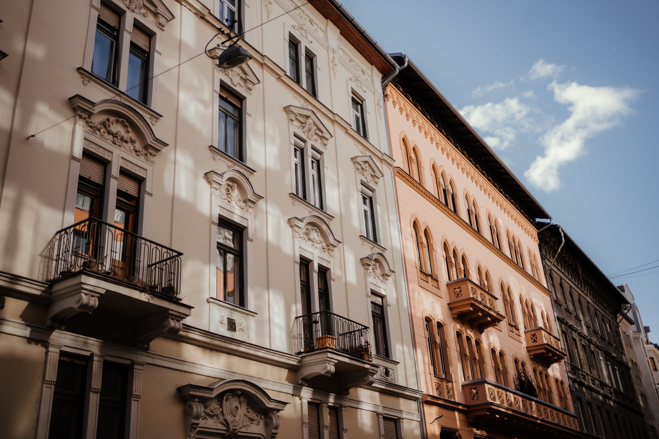 Historic European apartment buildings with decorative facades and wrought iron balconies in warm sunlight.