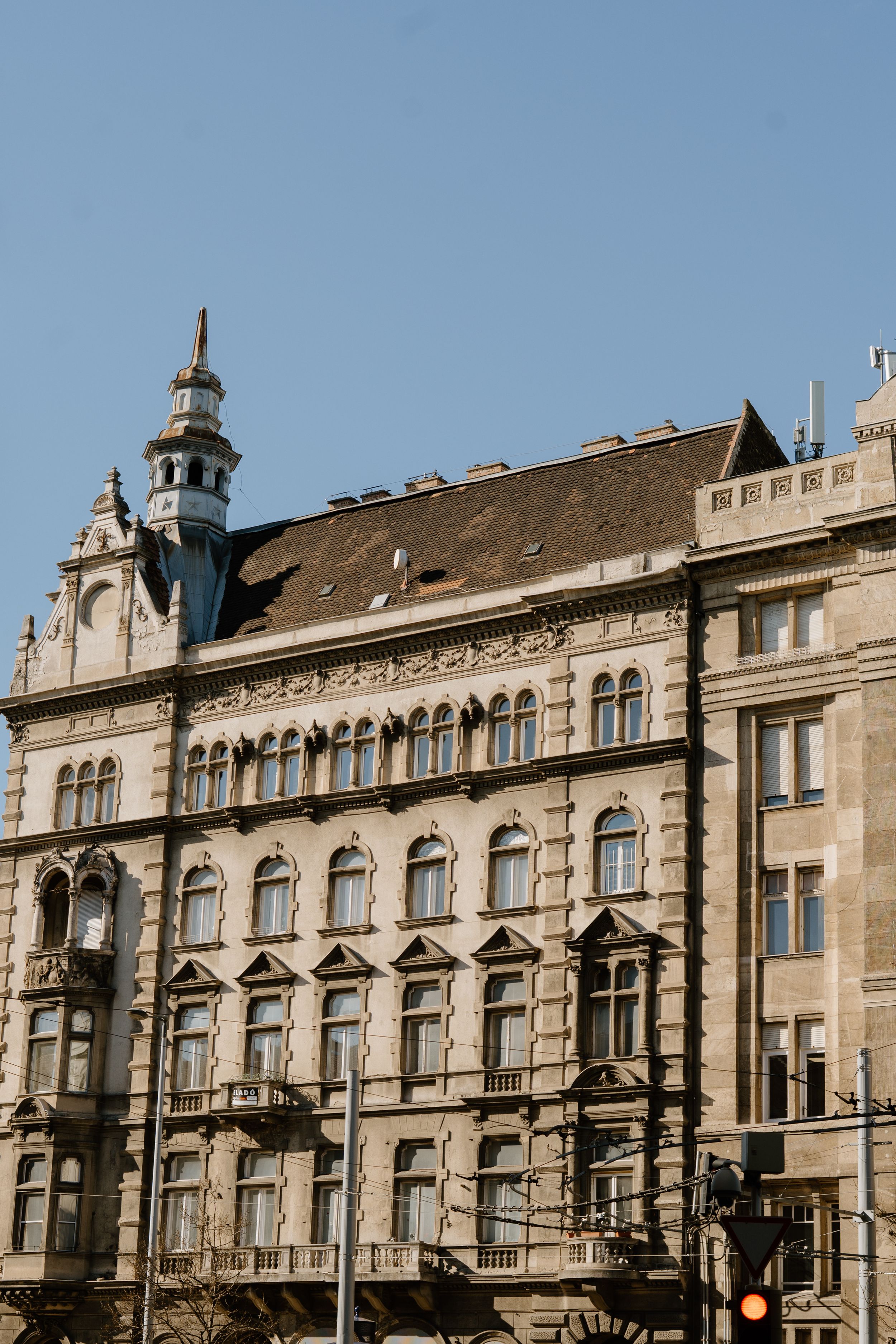 Ornate historic European apartment building with decorative facade and arched windows against blue sky in Budapest.