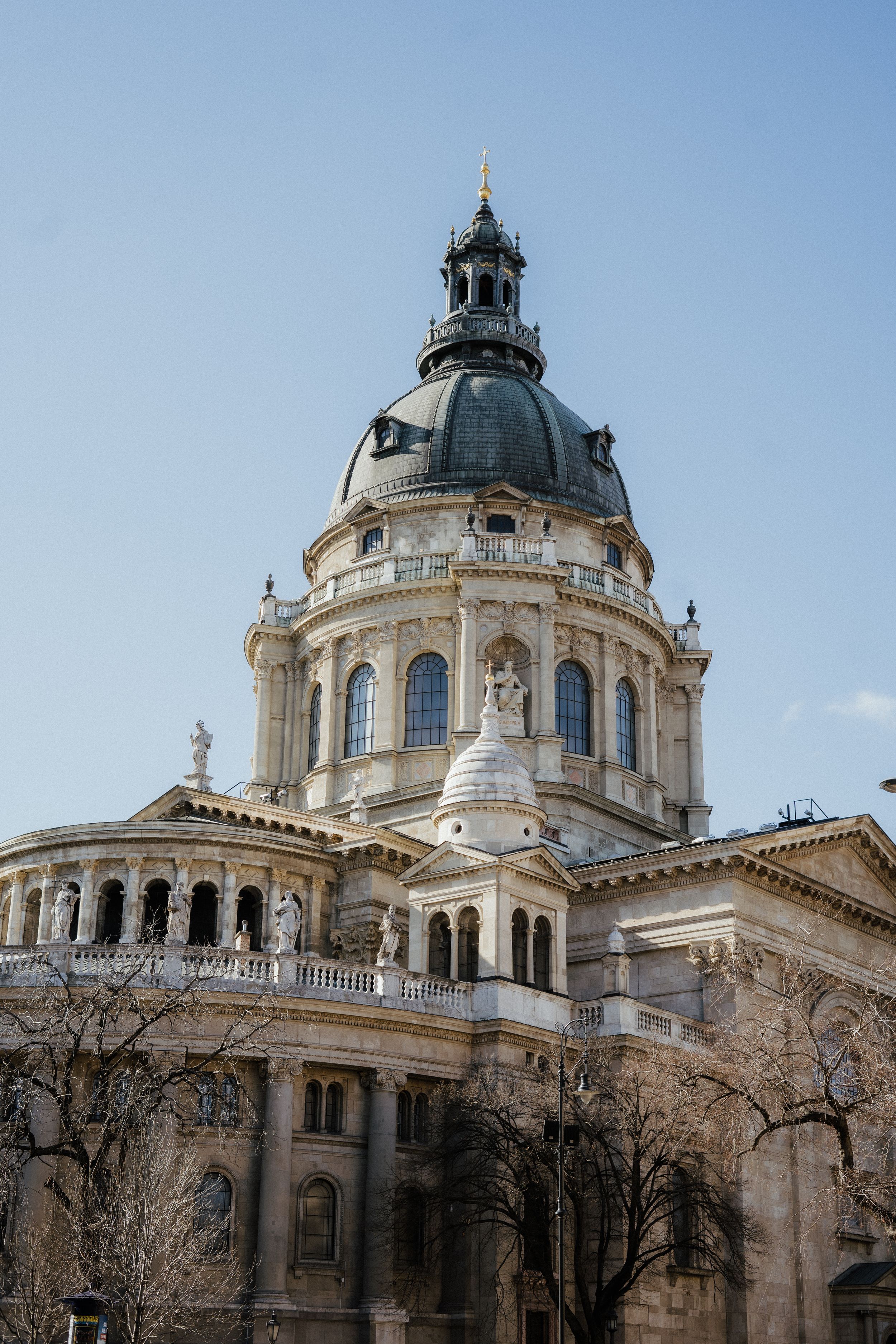 The ornate dome and classical architecture of the Budapest Basilica rises against a clear blue sky in Hungary.