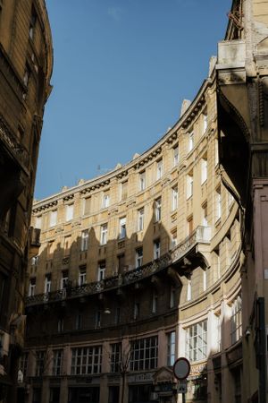 Curved neoclassical building facade with ornate windows and balconies casts dramatic shadows against bright blue sky in European city.
