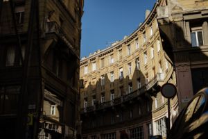 Curved historic building facade with ornate architecture and dramatic shadows cast across yellow walls in golden sunlight.