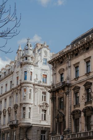 Ornate white and beige European architectural buildings with decorative facades and balconies against a blue sky in Budapest.