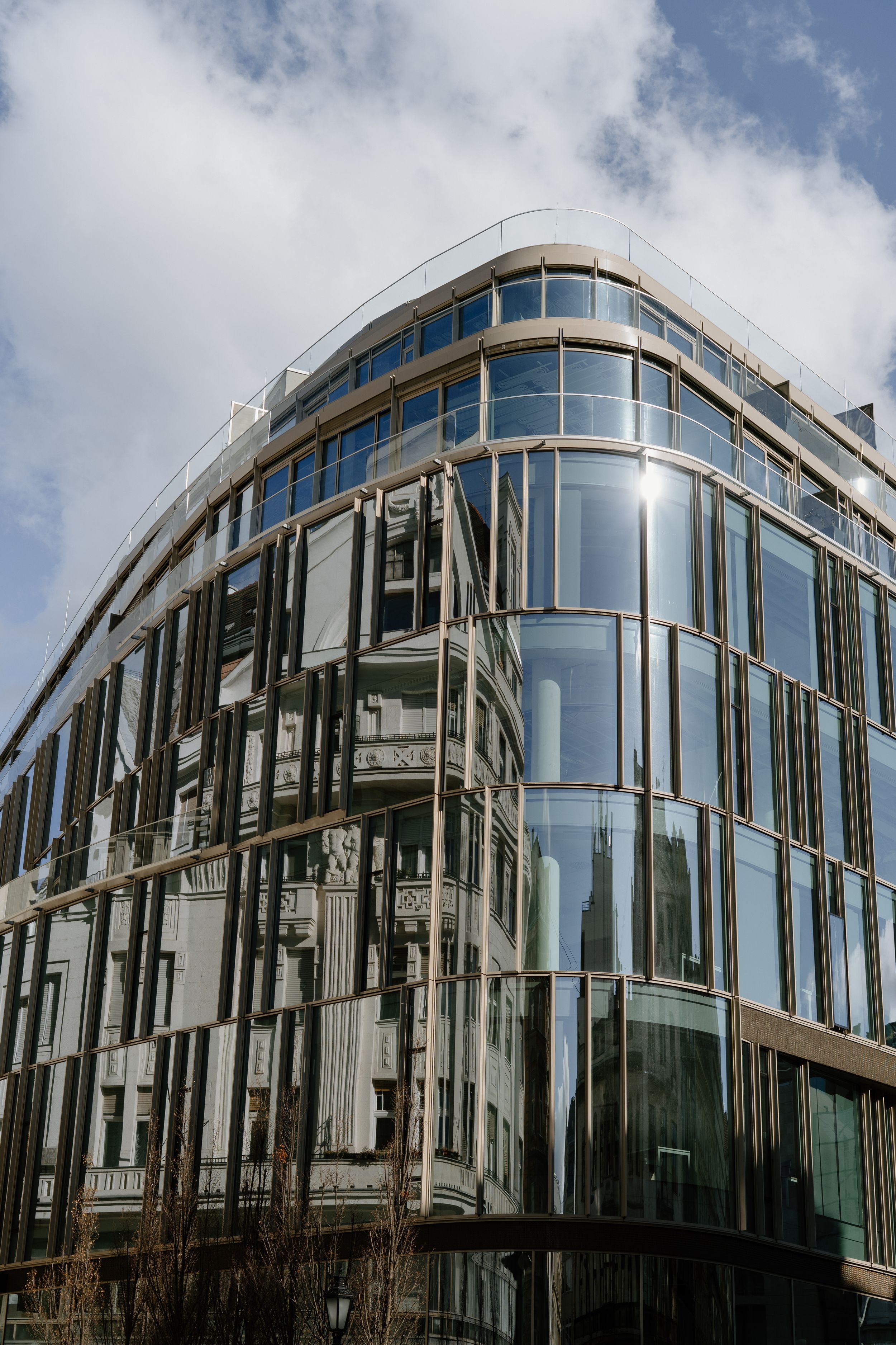 Modern curved glass office building with reflective windows and contemporary architectural design against cloudy sky.