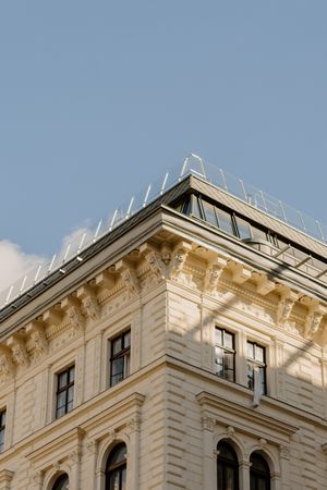 Ornate architectural detail of a classical building facade with decorative cornices and windows against a blue sky.