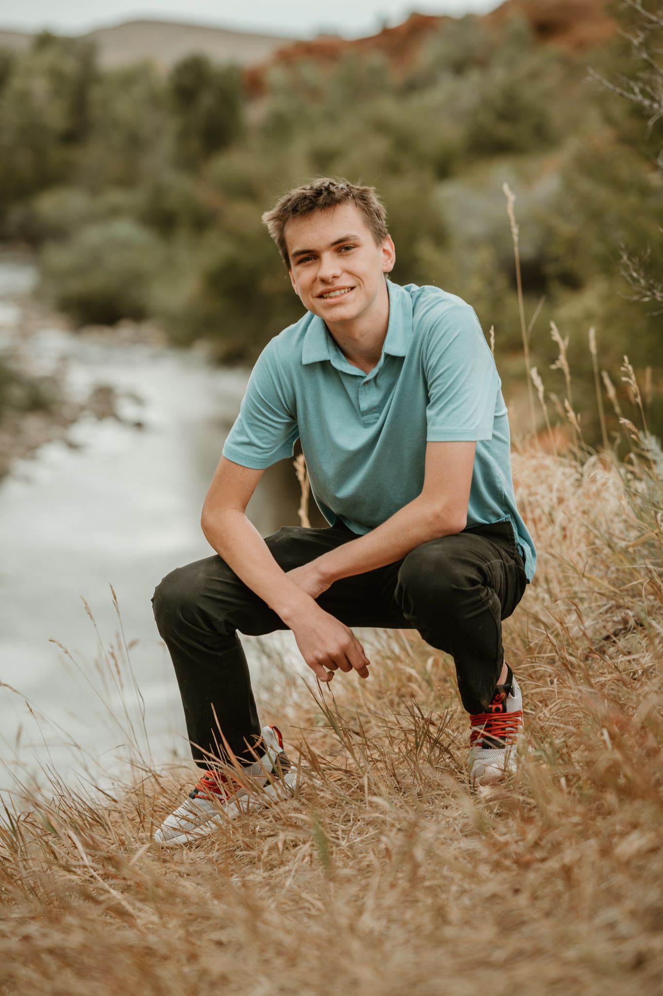 Person in teal polo shirt crouching in tall grass during golden hour.