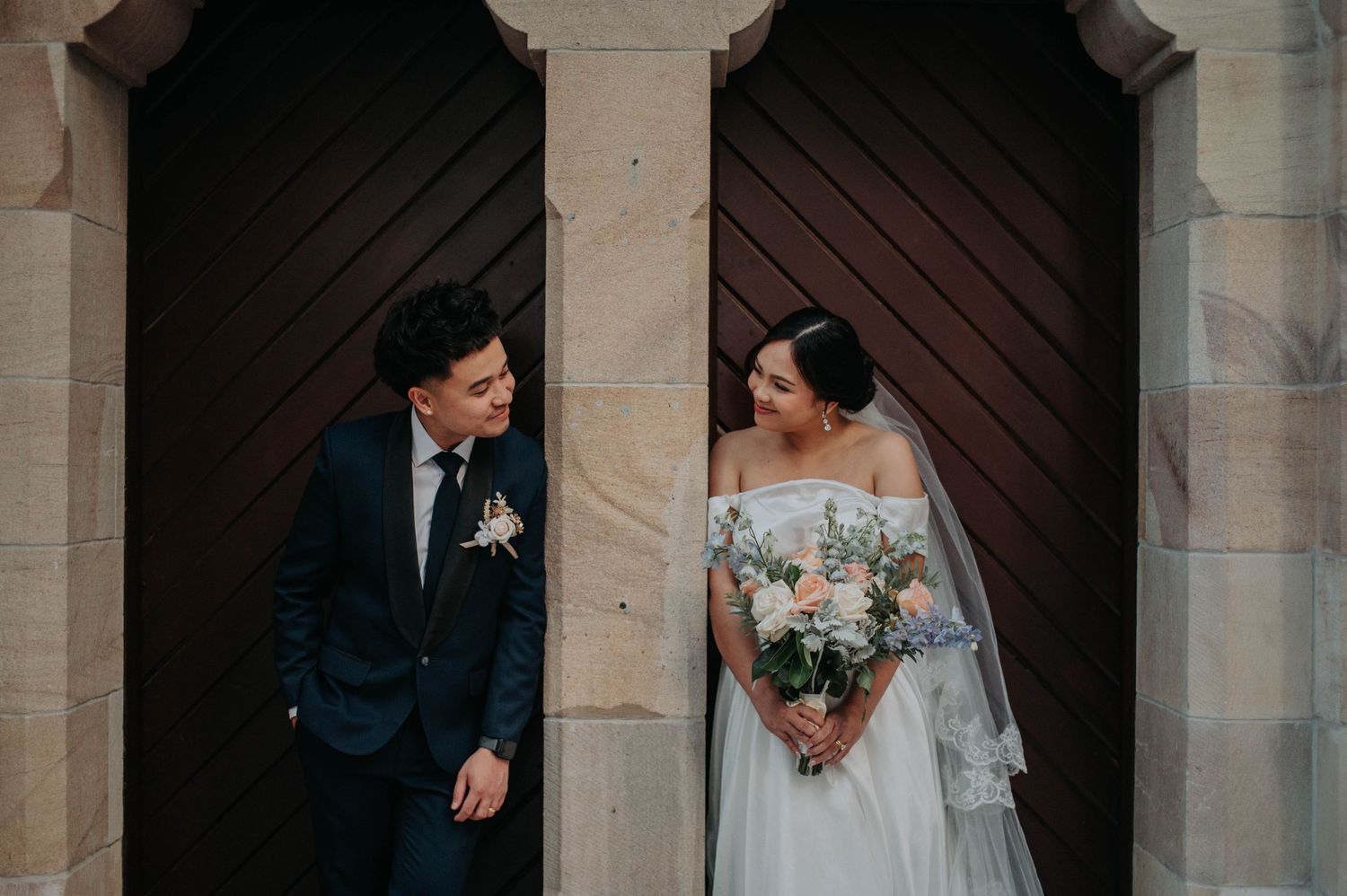 Candid portrait of newlyweds standing against wooden church doors.