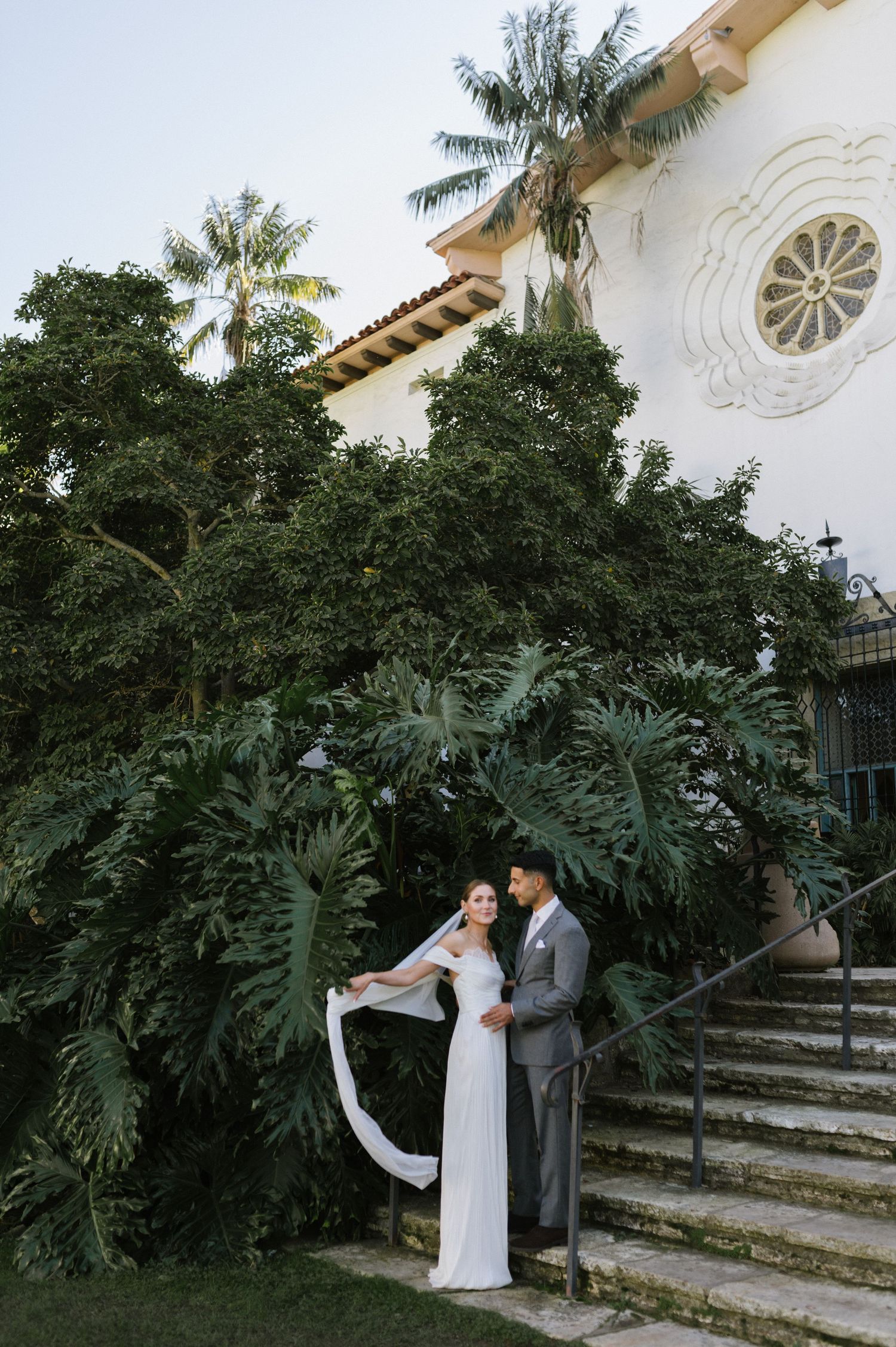 A romantic wedding portrait against lush tropical foliage and Spanish colonial architecture.