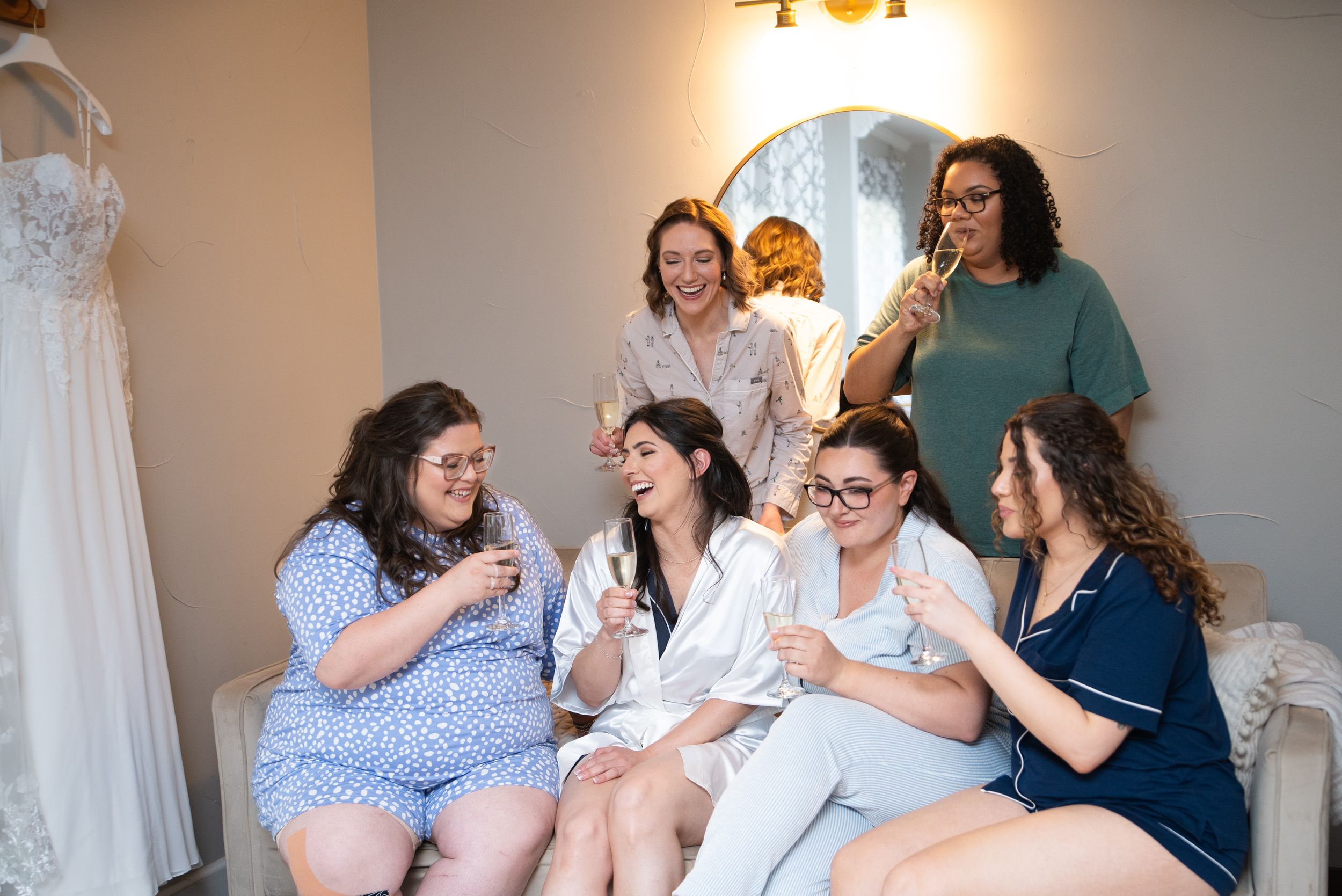 A group of friends laugh and share a joyful moment together while sitting on a couch in a bridal room.