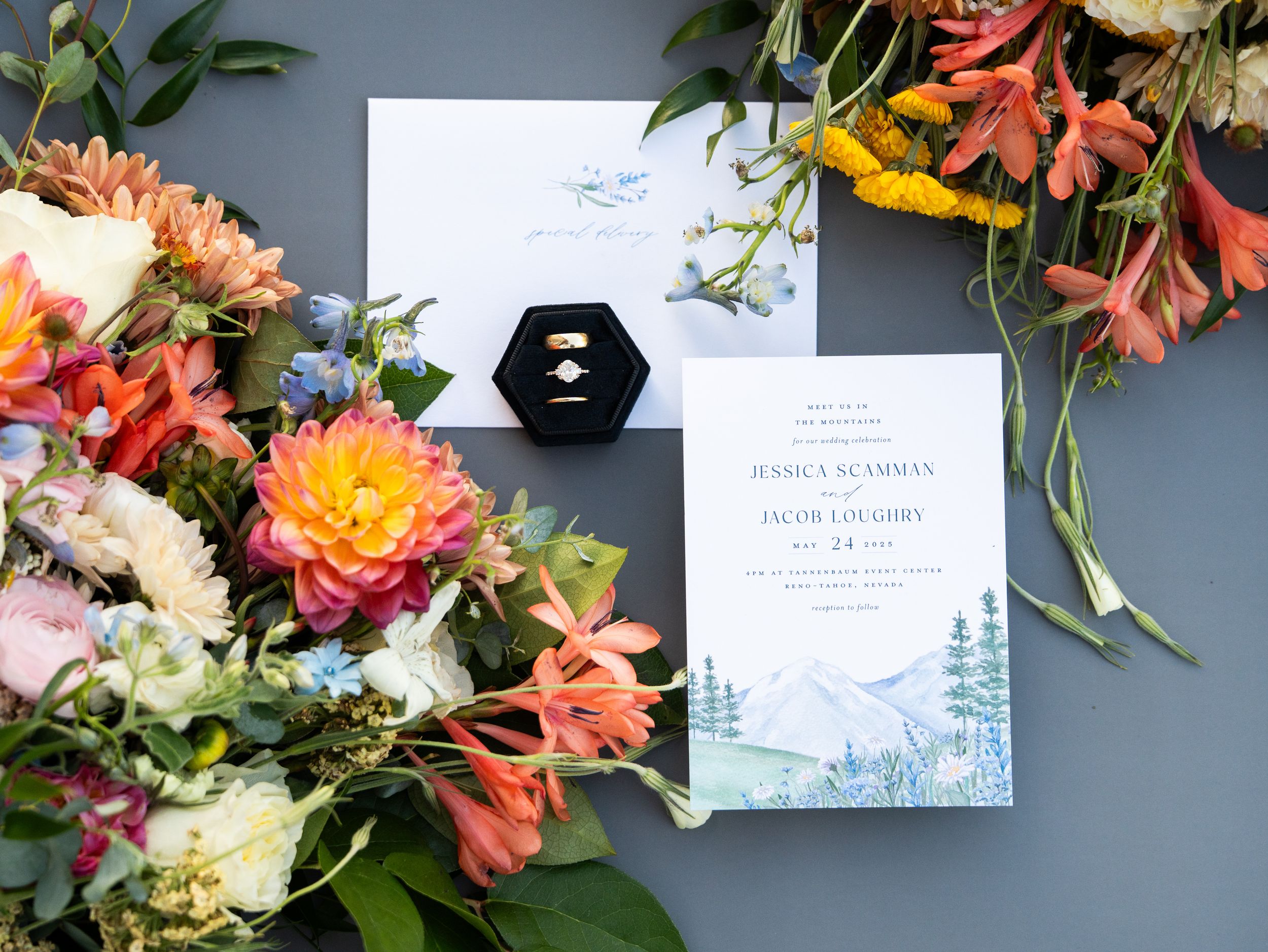 Colorful floral wedding stationery and decorative elements arranged on a grey surface with pink and orange blooms.
