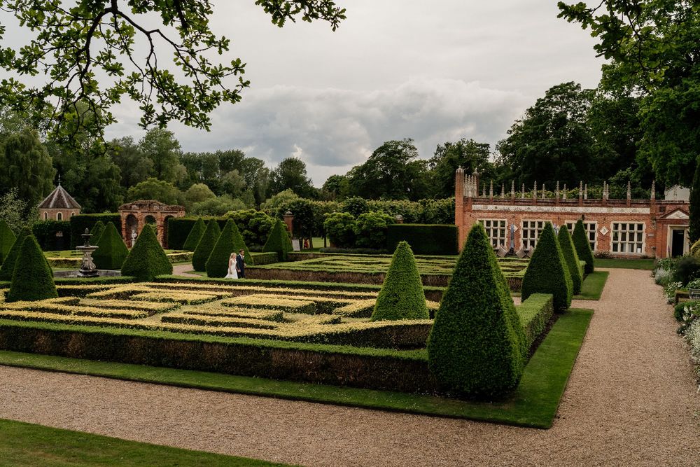 A panoramic view of a formal English garden at Oxnead Hall manicured hedges, topiary bushes, and a historic brick mansion in the distance.