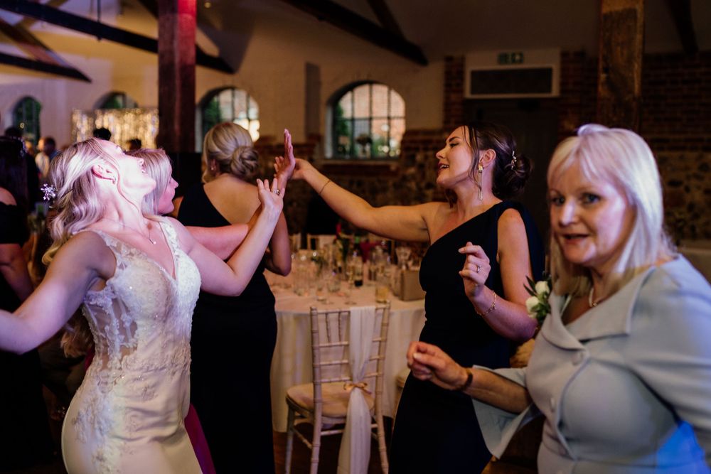 People dancing and enjoying themselves at an indoor wedding reception with brick walls and arched windows.