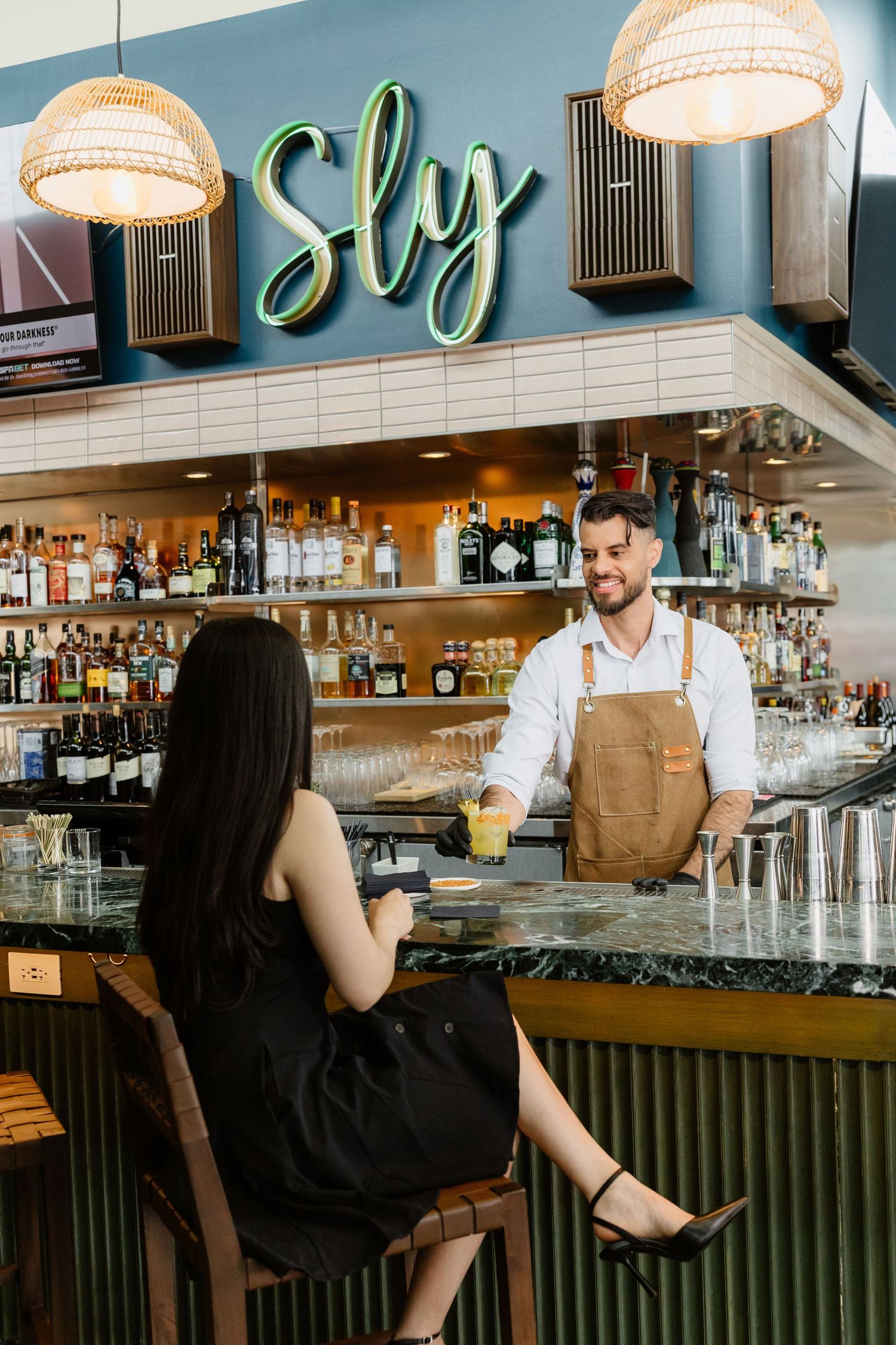 Modern bar interior with pendant lighting and industrial-style decor showing bartenders serving customers.