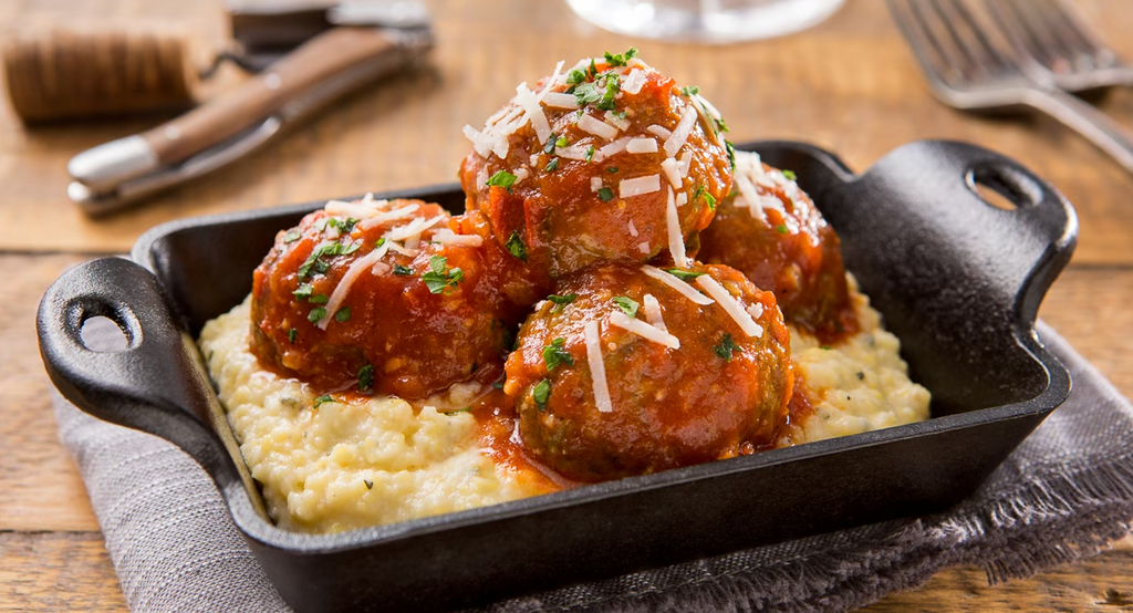 Meatballs in tomato sauce served over creamy polenta in a cast iron skillet.