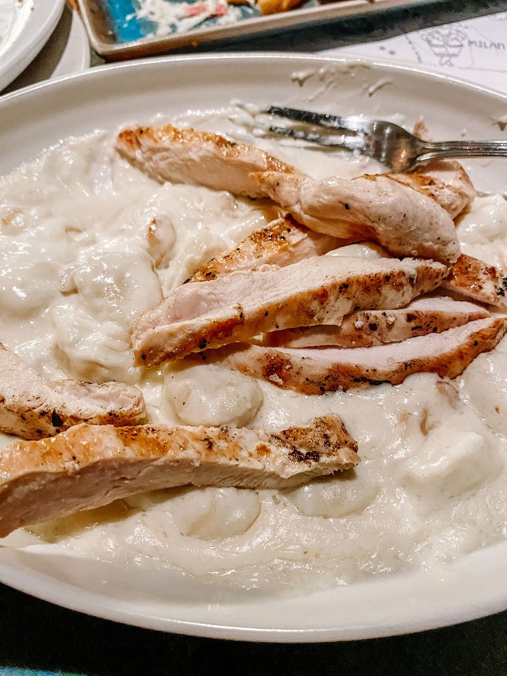 Grilled chicken breast served with creamy white sauce on a white plate.
