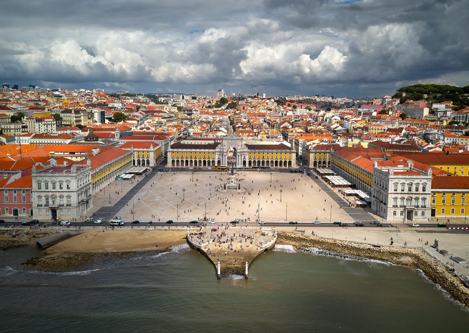 Aerial panorama of Lisbon's historic waterfront with Praca do Comercio square and terracotta rooftops.