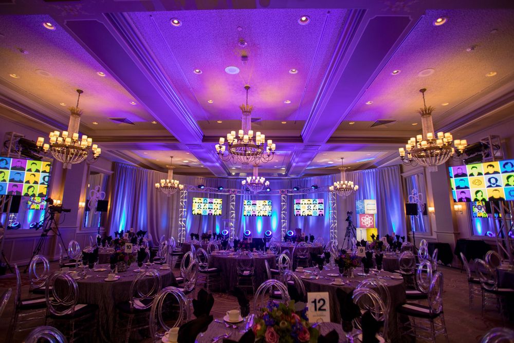 Elegant ballroom with purple uplighting, crystal chandeliers and round dining tables set for a formal evening event.