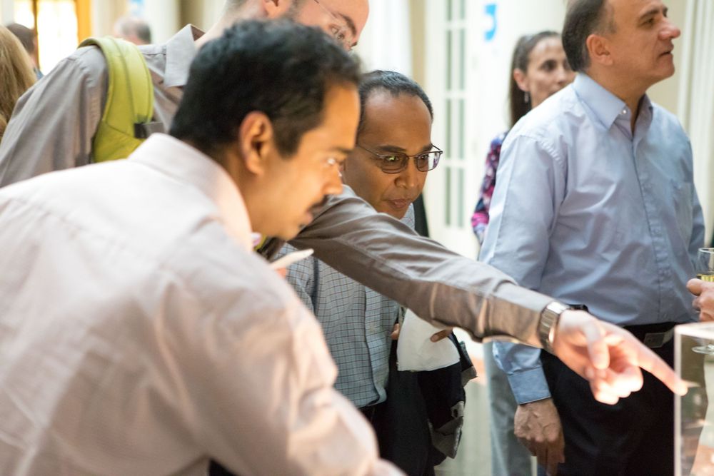 Colleagues interact during a meeting in an office hallway, pointing and discussing together.