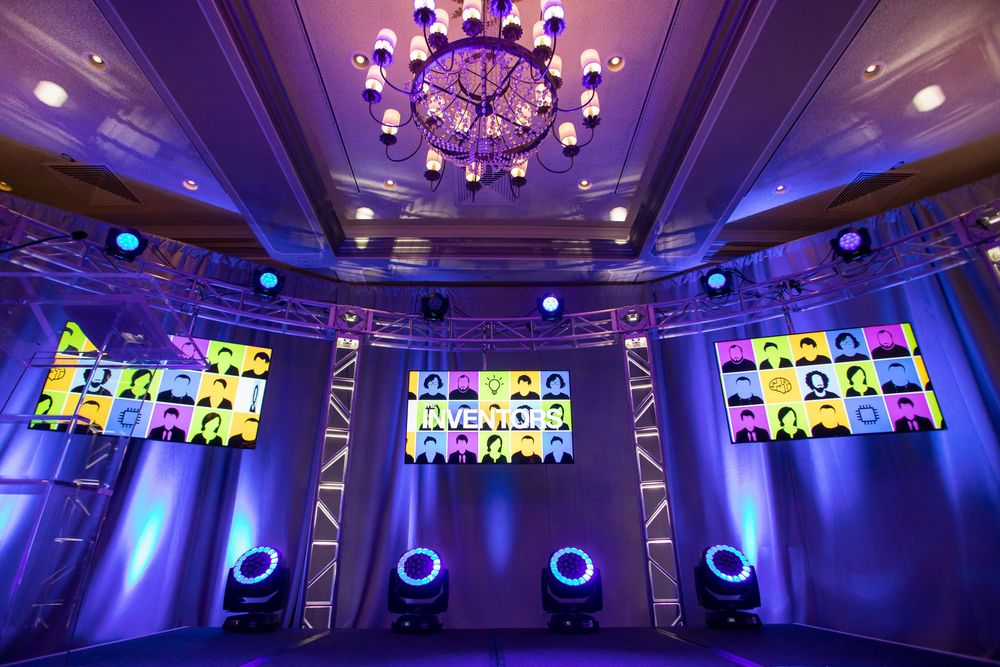 Panoramic view of an elegant event ballroom with purple mood lighting and ornate crystal chandeliers illuminating the space.