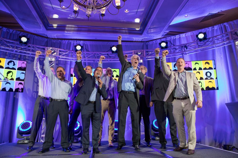 Group of business professionals standing in formation under purple lighting at a corporate event.