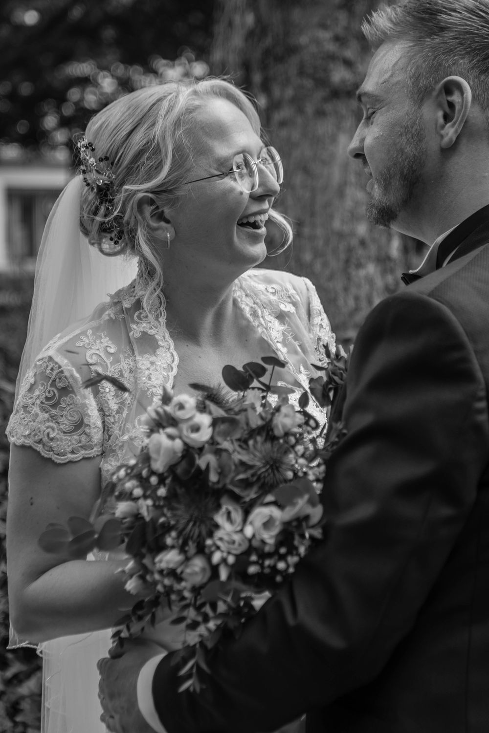 Black and white wedding photo of a happy couple sharing a joyful moment with the bride holding a floral bouquet.