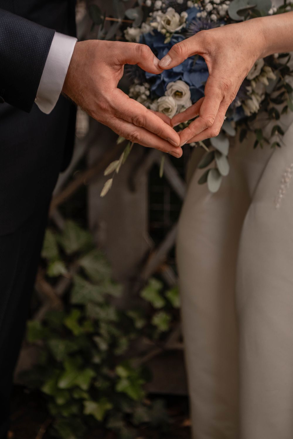 Close-up of hands exchanging wedding rings during an intimate ceremony with blurred floral backdrop.