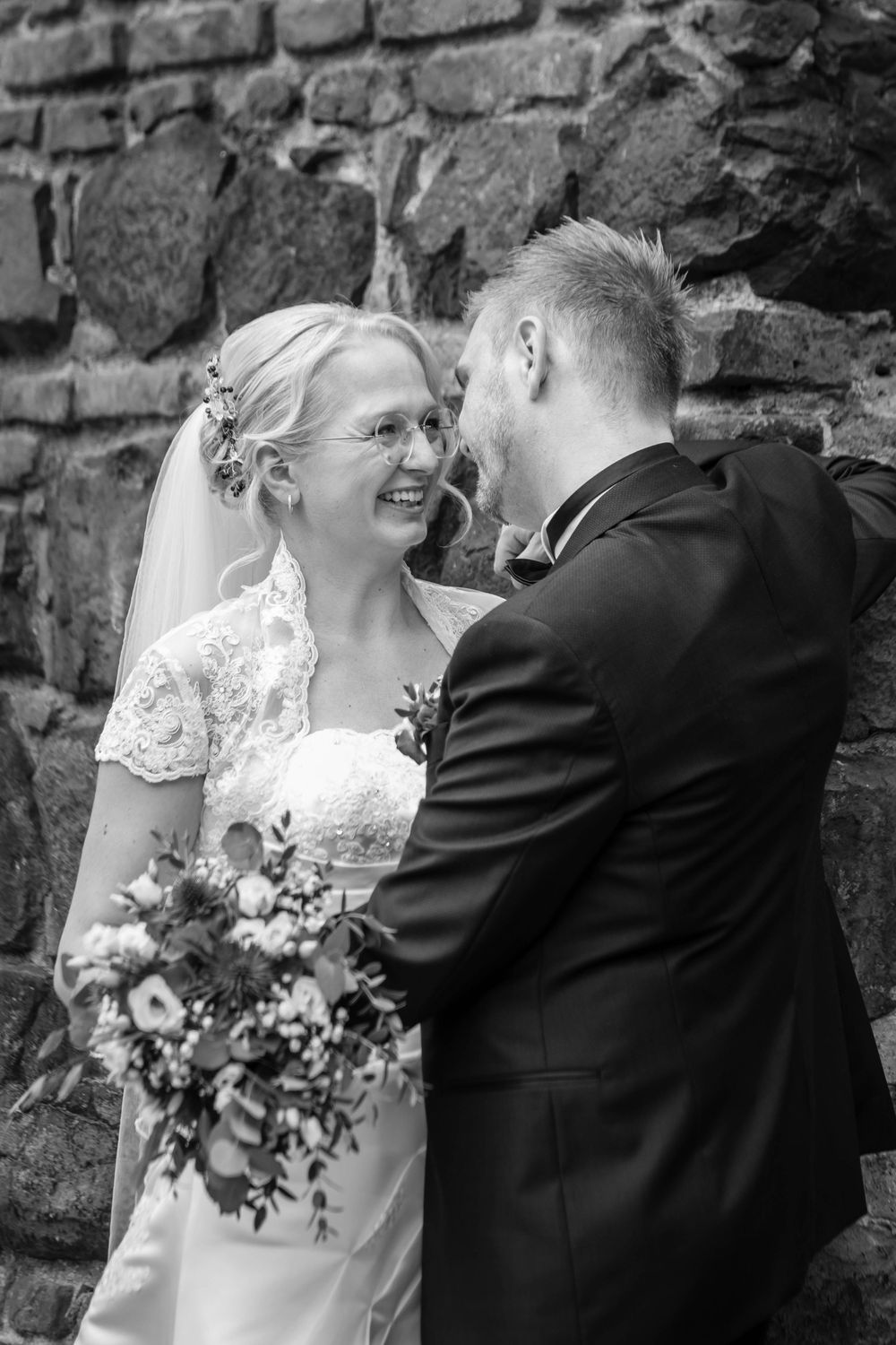 A romantic sequence of black and white wedding photos showing a couple embracing beside a stone wall.