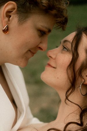 Close-up of two brides sharing an intimate moment, nearly touching foreheads, smiling softly.