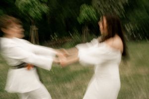 A motion-blurred photo of a couple in white outfits holding hands and spinning in a garden.