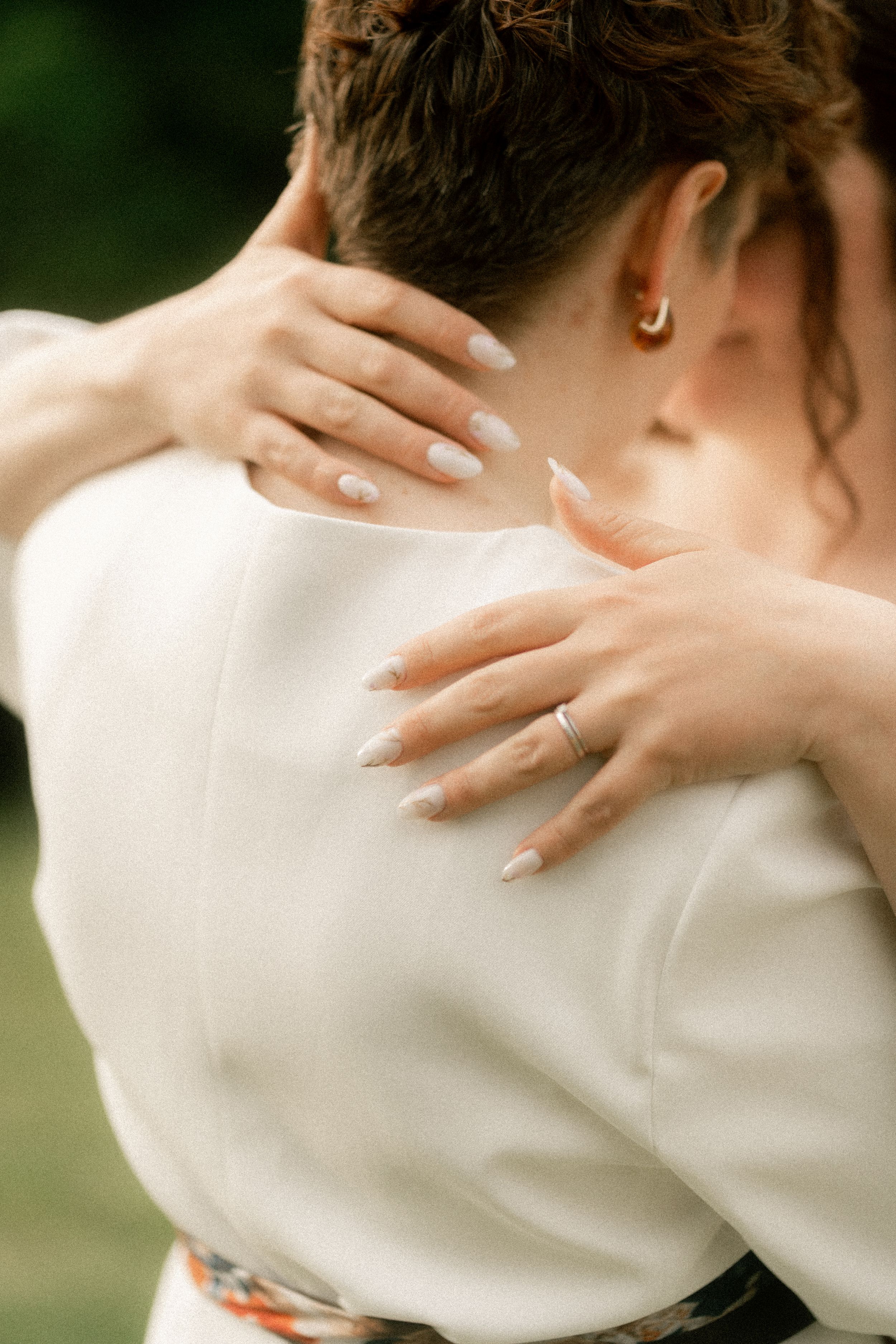 Close-up of bride hugging groom, showcasing French manicure nails and diamond wedding ring against white suit.