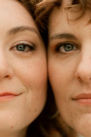 Close-up portrait of two women with blue eyes and light skin smiling cheek to cheek.