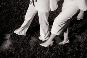 Barefoot couple in white outfits walking on wet pavement, black and white wedding photo.