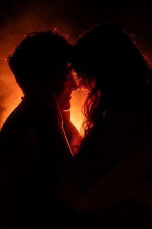 Romantic silhouette of a couple about to kiss against a glowing red and orange fire backdrop.