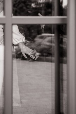 Black and white photo of two people holding hands through a glass window reflection.