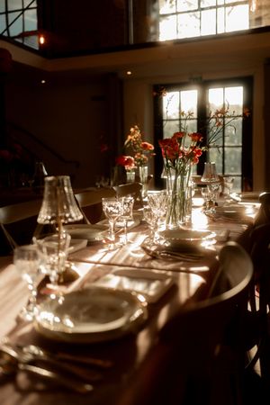 Elegant wedding reception table set with crystal glasses, white plates, and red floral centerpieces in warm sunlight.