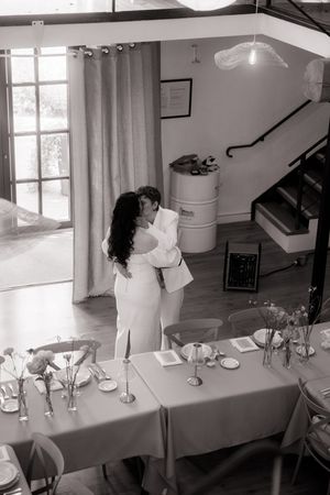 Aerial black and white photo of couple sharing first kiss in decorated wedding reception hall.