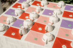 Colorful wedding place cards in red, pink, and purple with white ceramic favor boxes arranged on a table.