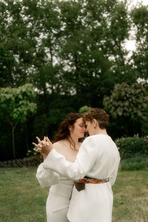 A couple in white wedding attire embracing and dancing together in a lush green garden.