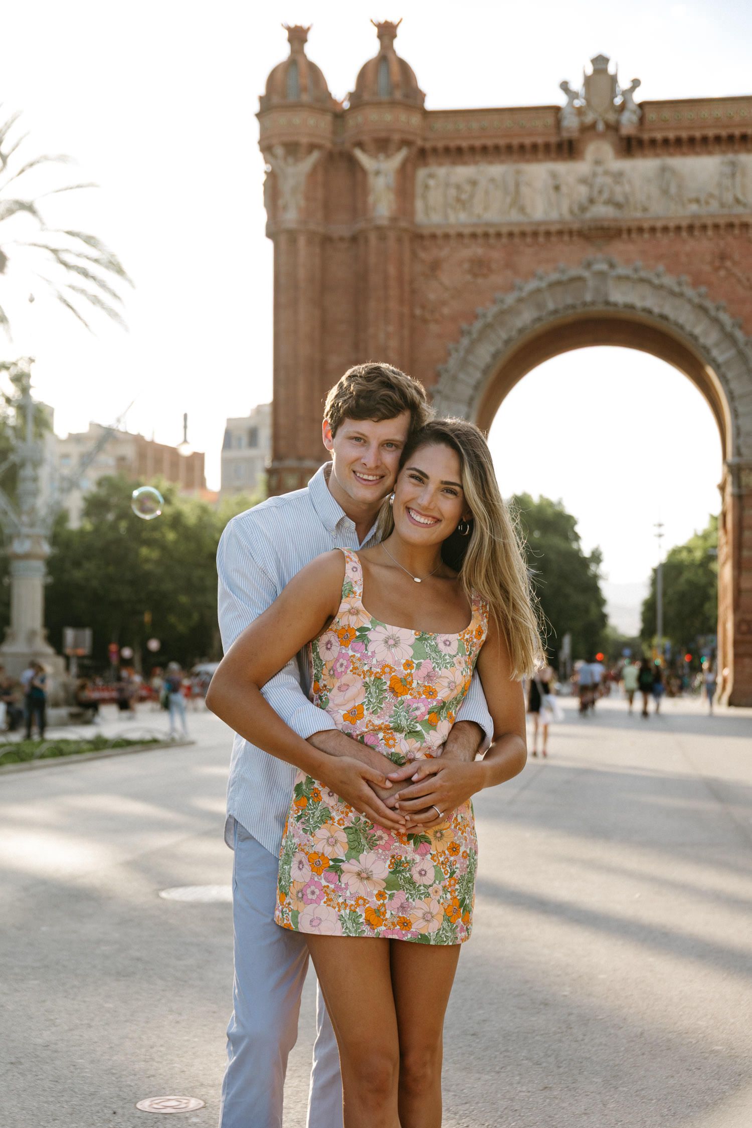 Happy couple embraces in front of ornate arch monument during golden hour.