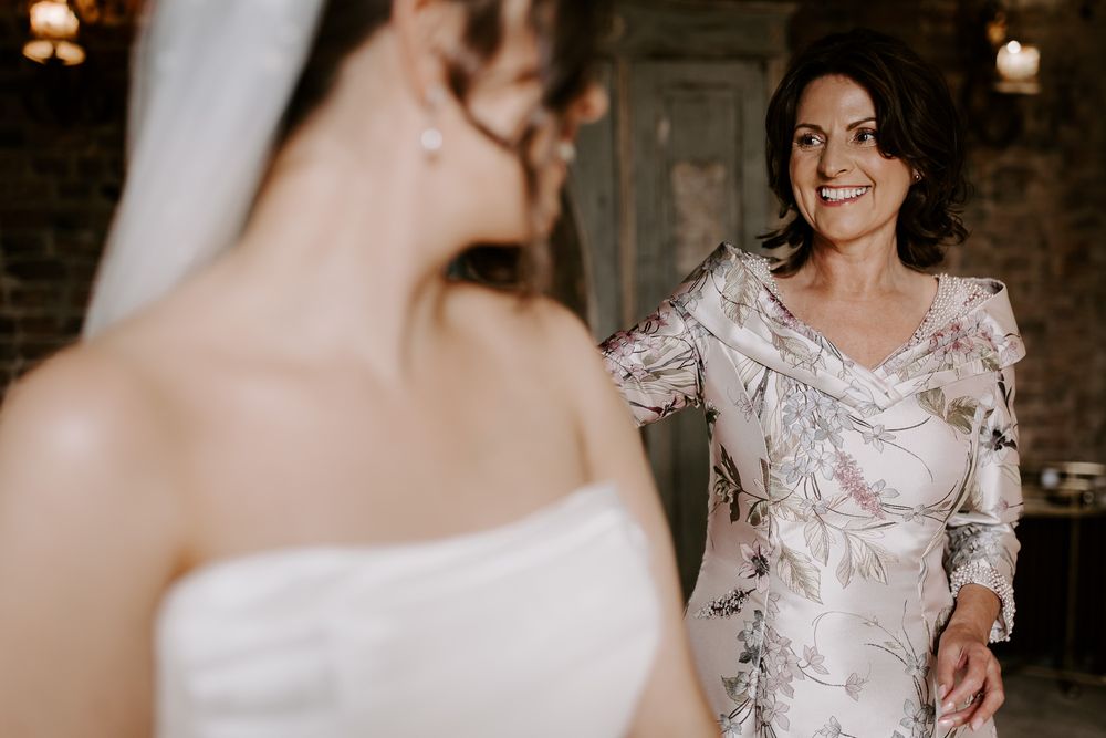 Two women in elegant white lace dresses during a special occasion in a dimly lit rustic setting.