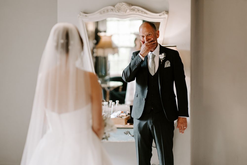 An emotional first look moment captured at an indoor wedding as a person reacts to seeing their bride in her white veil.