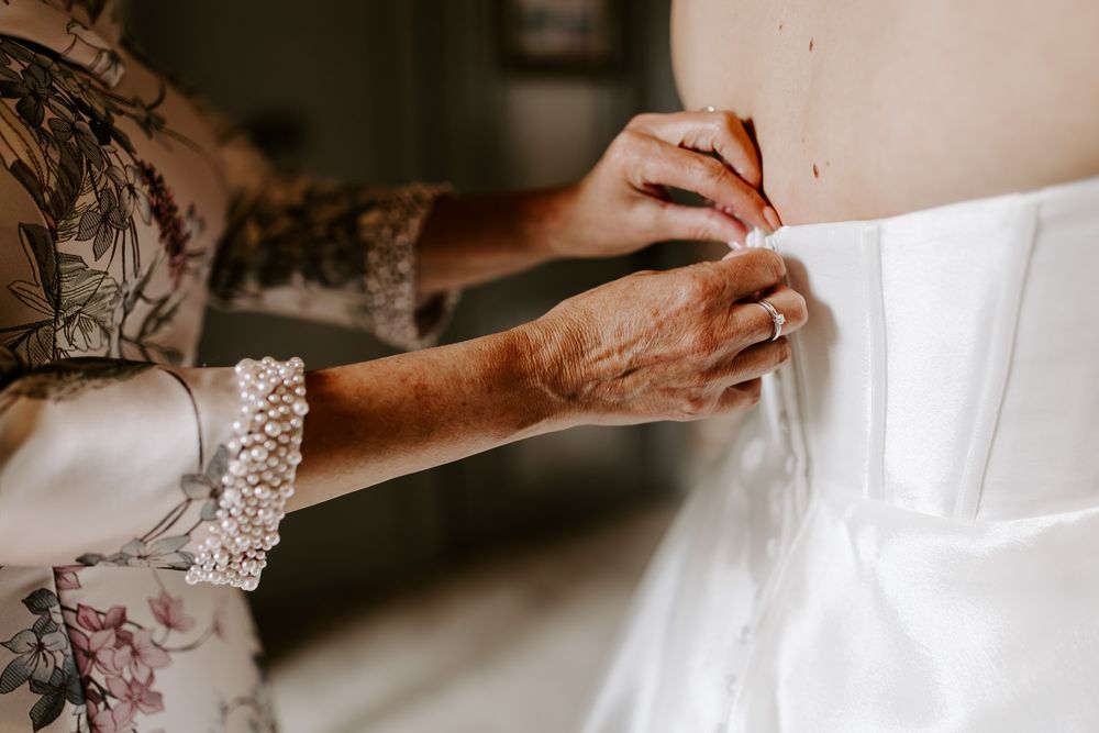 Close-up view of hands buttoning up a white wedding dress with delicate lace details.