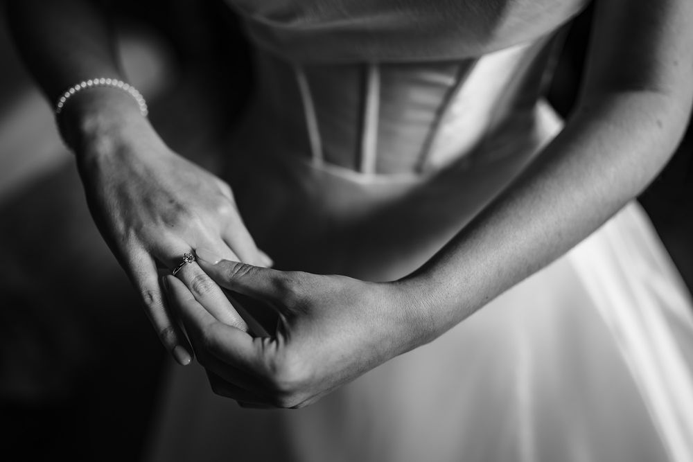 A black and white close-up of hands adjusting a delicate bracelet against the fabric of a white dress.