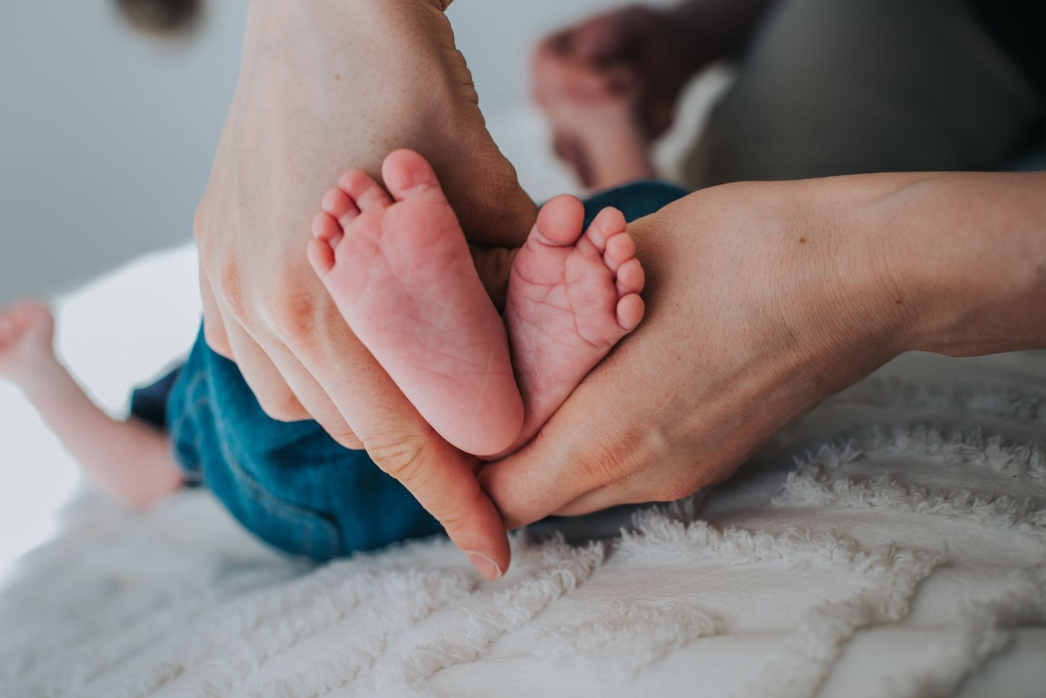 Gentle hands hold tiny baby feet against a soft white textured blanket.