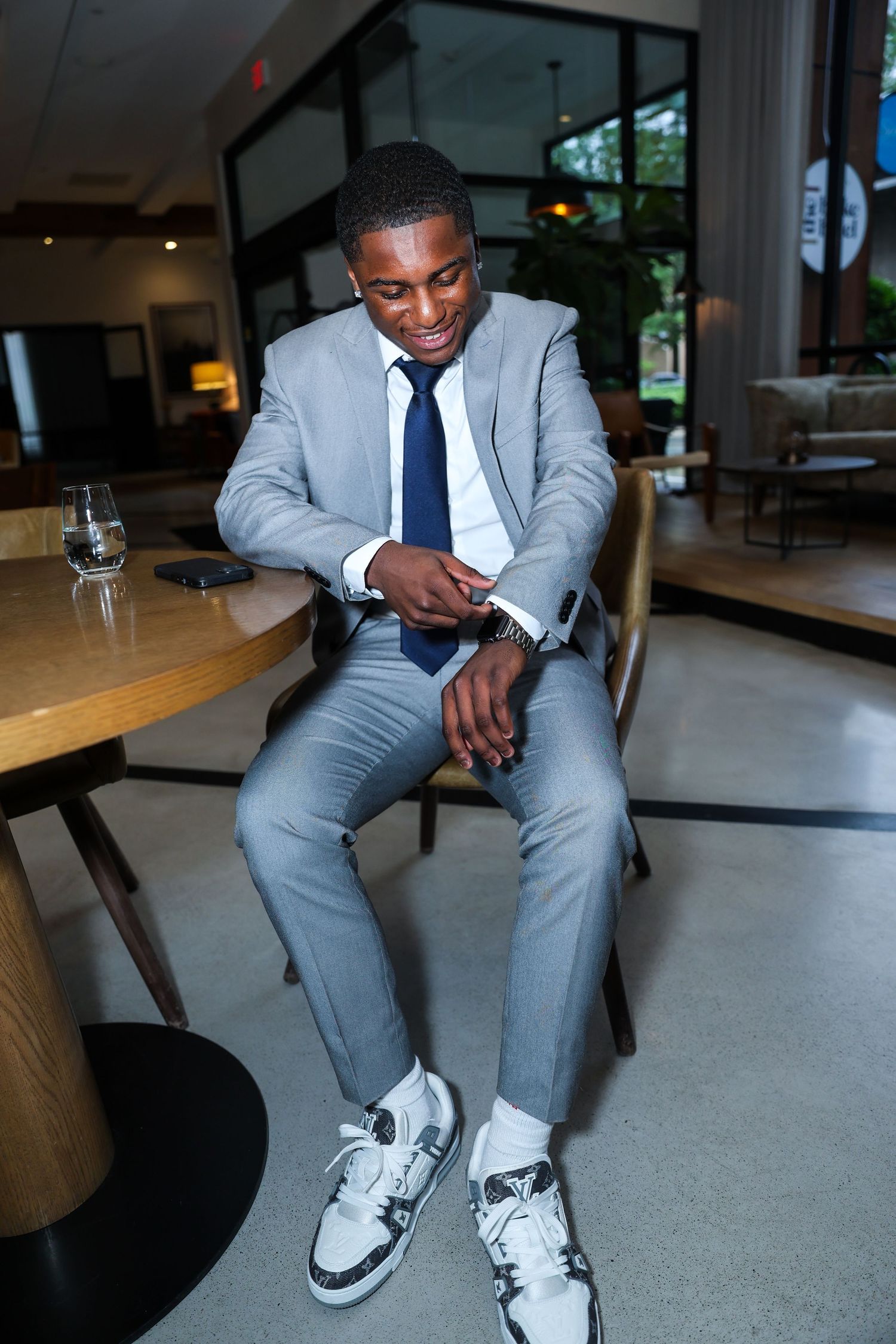Professional in gray suit checks watch while seated in modern restaurant.