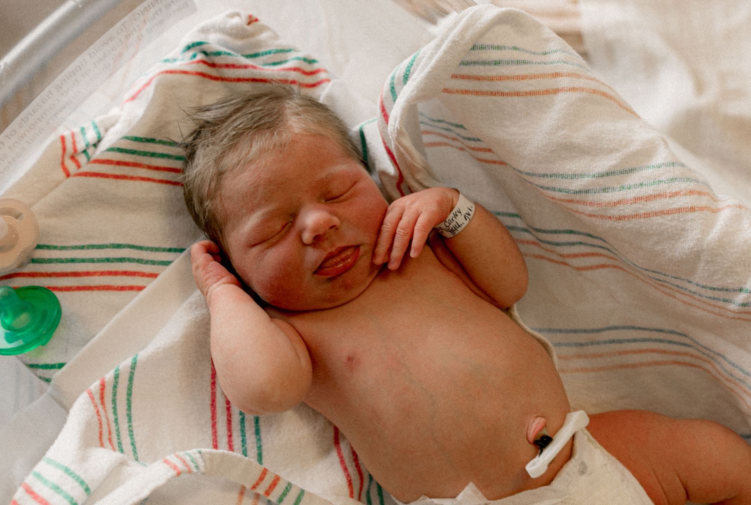 A newborn baby sleeping peacefully on striped linens with a hospital identification band visible.