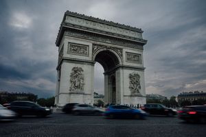L’Arc de Triomphe à Paris sous un ciel dramatique, avec voitures en mouvement sur les Champs-Élysées.