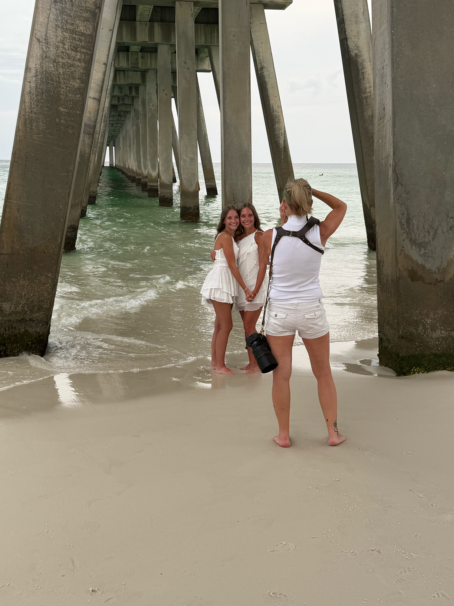 People standing beneath a pier on the beach while turquoise waves roll in between the concrete supports.